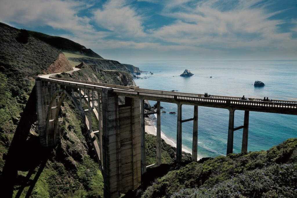 Iconic Pacific Highway bridge in California, showcasing breathtaking outdoor adventure with hills, blue waters of the Pacific Ocean, and stunning bridge opening view.
