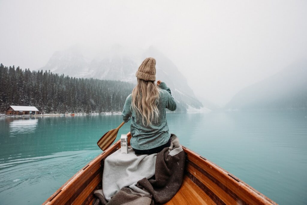 Young female paddling a canoe on a misty mountain lake, embracing the outdoor adventure amidst serene blue waters and distant mist-covered mountains